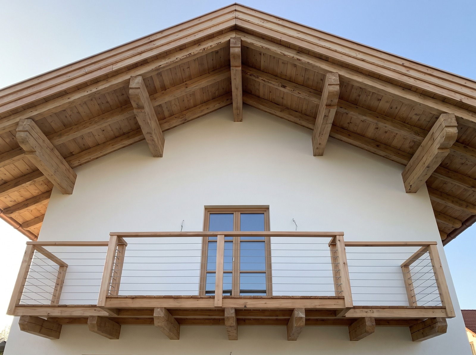 Giebel eines neu gebauten Hauses mit weit überstehendem Dach und einem Balkon aus Lärchenholz